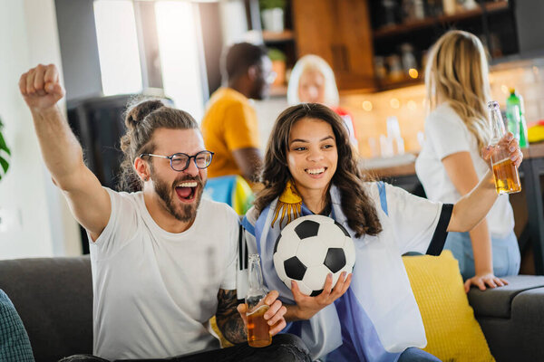 Возбужденная группа молодых мультиэтнических людей, смотрящих футбол по телевизору дома
