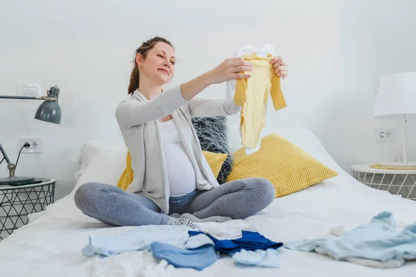Beautiful Young Smiling Pregnant Woman Looking Cute Baby Clothes — Stock Photo, Image