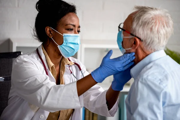 女医は診療所で男性高齢者の診察をしている 顔のマスクをした医者と患者 — ストック写真