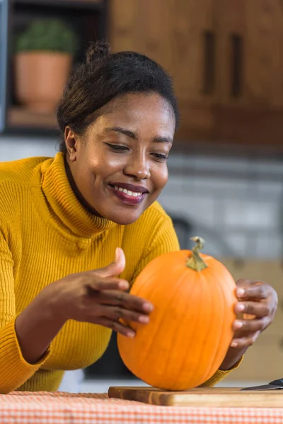 Młoda Uśmiechnięta Czarna Kobieta Przygotowuje Się Halloween Rzeźbiąc Dynię Domu — Zdjęcie stockowe