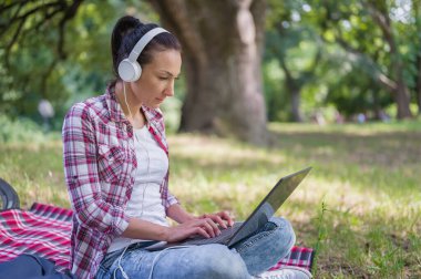 Bilgisayarda çalışan bir kadın halka açık bir parkta çimlerin üzerinde oturuyor.