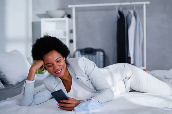 stock image Young black businesswoman just arrived at the hotel taking a rest from a trip, using a smartphone