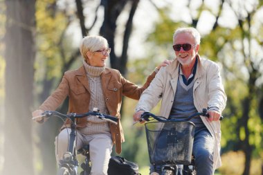 Bisikletleriyle parka gidip eğlenen neşeli, aktif son sınıf çifti. Yaşlılar için mükemmel aktiviteler. Parkta bisiklet süren mutlu, olgun bir çift.