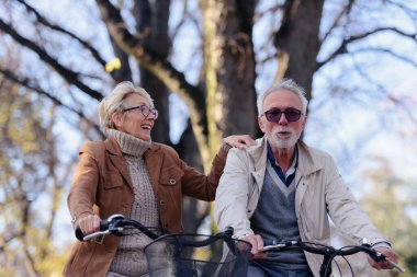 Bisikletleriyle parka gidip eğlenen neşeli, aktif son sınıf çifti. Yaşlılar için mükemmel aktiviteler. Parkta bisiklet süren mutlu, olgun bir çift.