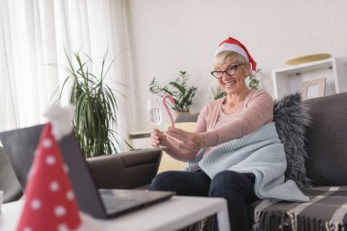 Noel Baba şapkası takan, evde şampanya içen, bilgisayara doğru kadeh kaldıran yaşlı bir kadın. Tatillerde ailemle internet üzerinden video görüşmeleri yapıyorum..