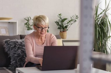 Güzel yaşlı kadın ailesiyle iletişim kurmak için dizüstü bilgisayar kullanıyor, internette sörf yapıyor, internetten alışveriş yapıyor, kahve içiyor.