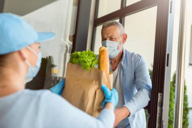 Teslimatçı kız COVID salgını sırasında yaşlı bir adama erzak getiriyor. İnsanlar koruyucu maskeler takıyor..