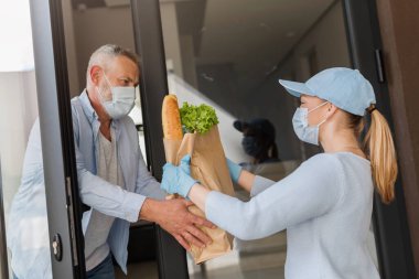 Teslimatçı kız COVID salgını sırasında yaşlı bir adama erzak getiriyor. İnsanlar koruyucu maskeler takıyor..