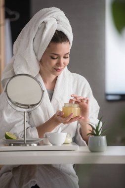 Evde bornoz giyen güzel bir kadının portresi. Günlük cilt bakımını doğal kozmetiklerle yapıyor.