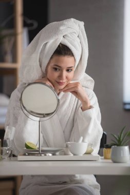 Evde bornoz giyen güzel bir kadının portresi. Günlük cilt bakımını doğal kozmetiklerle yapıyor.