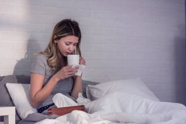 Hasta olduğu için evde. Kadının soğuk algınlığı var. Öksür. Soğuk algınlığına ya da gribe yakalanmış güzel genç bir kadının yakın çekimi. Boğazında Ağrı Olan Sağlıksız Bir Kızın Portresi.