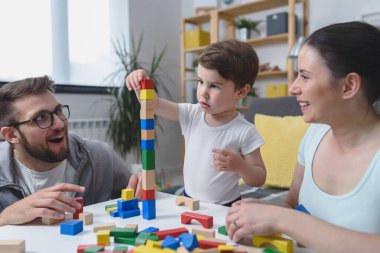 Genç ve mutlu bir aile. Anne ve baba, küçük tatlı oğluyla evde didactik tahta oyuncaklar kullanarak oynuyorlar. Evde eğitim