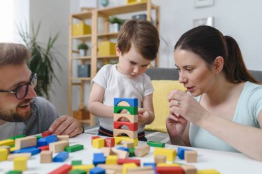 Genç ve mutlu bir aile. Anne ve baba, küçük tatlı oğluyla evde didactik tahta oyuncaklar kullanarak oynuyorlar. Evde eğitim