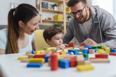 Genç ve mutlu bir aile. Anne ve baba, küçük tatlı oğluyla evde didactik tahta oyuncaklar kullanarak oynuyorlar. Evde eğitim