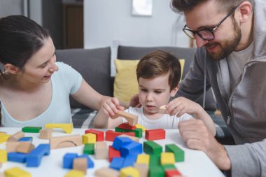 Genç ve mutlu bir aile. Anne ve baba, küçük tatlı oğluyla evde didactik tahta oyuncaklar kullanarak oynuyorlar. Evde eğitim
