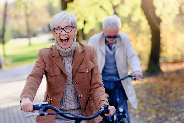 Cheerful active senior couple with bicycles in public park together having fun. Perfect activities for elderly people. Happy mature couple riding bicycles in park