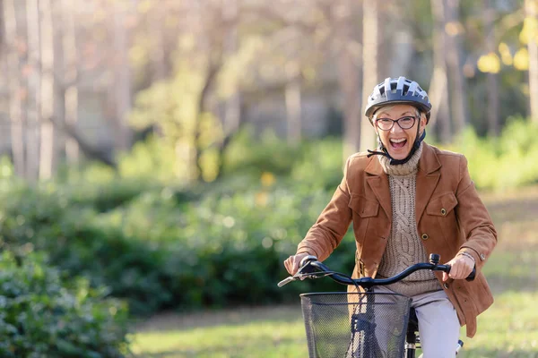 Cheerful elderly woman riding bicycle in public park. Activities for older people