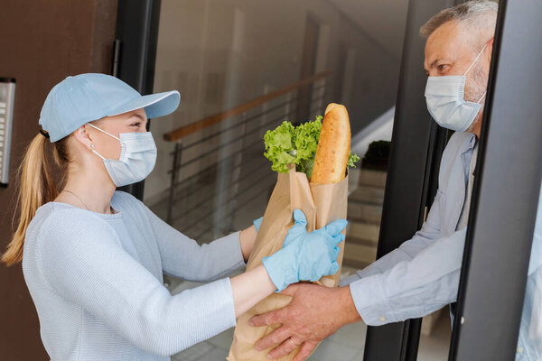 Delivery service girl brings groceries to an elderly man during COVID pandemic. peole wearing protective masks.
