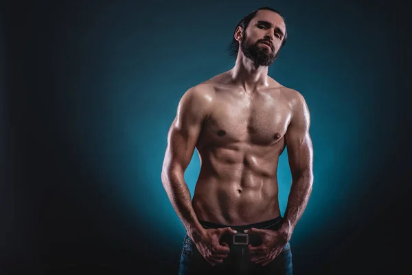 Studio portrait of a beautiful masculine bearded shirtless man showing his abdomen muscles