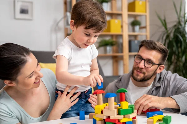 Genç ve mutlu bir aile. Anne ve baba, küçük tatlı oğluyla evde didactik tahta oyuncaklar kullanarak oynuyorlar. Evde eğitim