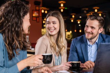 Tablet kullanan ve kafede otururken gülümseyen iki genç kadın ve erkek.  