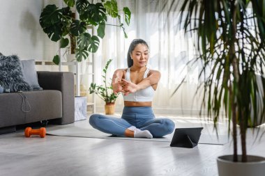 Genç Asyalı kadın yoga eğitmeni online yoga sınıfında tablet bilgisayar kullanıyor.