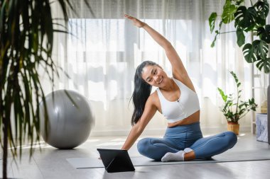 Genç Asyalı kadın yoga eğitmeni online yoga sınıfında tablet bilgisayar kullanıyor.