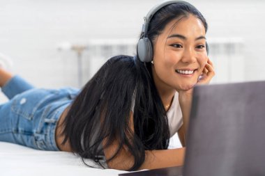 Asyalı bir öğrenci, evde internet üzerinden İngilizce öğrenen genç bir kadın. Kulaklık ve dizüstü bilgisayar kullanarak, online bir derse katılarak.