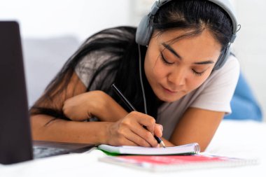 Asyalı bir öğrenci, evde internet üzerinden İngilizce öğrenen genç bir kadın. Kulaklık ve dizüstü bilgisayar kullanarak, online bir derse katılarak.