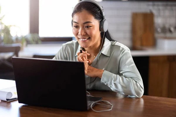 オンライン外国語の授業に参加する若いアジアの女性 ヘッドフォンでノートパソコンの前に座り コースを聞いてメモを取る — ストック写真