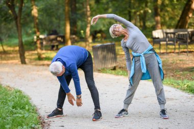 Spor giyimli genç bir çift parkta esneme egzersizleri yapıyor. 