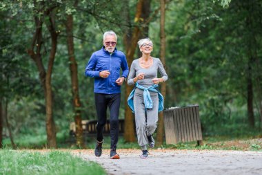 Mutlu yaşlı çift parkta koşuyor.