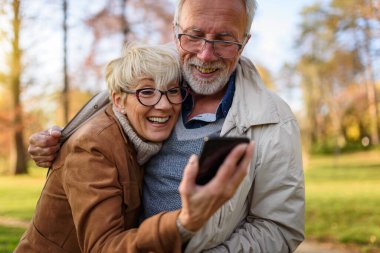 Mutlu yaşlı çift parkta selfie çekiyor.