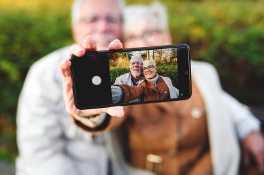 Mutlu yaşlı çift parkta selfie çekiyor.