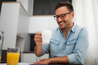 Evde bir fincan kahvesi olan yakışıklı bir genç adam.