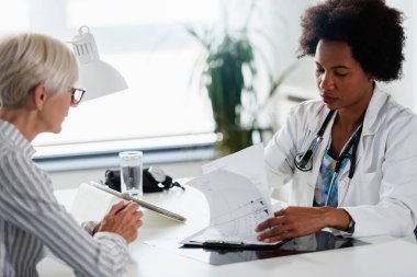 Afrikalı Amerikalı doktor, yaşlı kadın hastayı muayene ediyor.