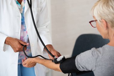 Afrikalı Amerikalı doktor, yaşlı kadın hastayı muayene ediyor.