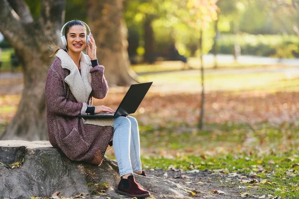 Νεαρή Γυναίκα Φορητό Υπολογιστή Και Ακουστικά Κάθεται Στο Πάρκο — Φωτογραφία Αρχείου