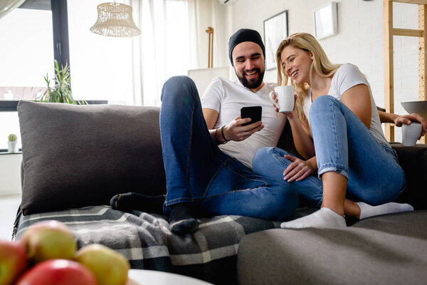 Young hipster couple sitting on sofa at home talking and drinking coffee