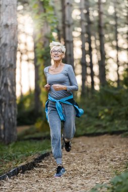 Gülümseyen yaşlı kadın parkta koşuyor. Yaşlılar için spor faaliyetleri.