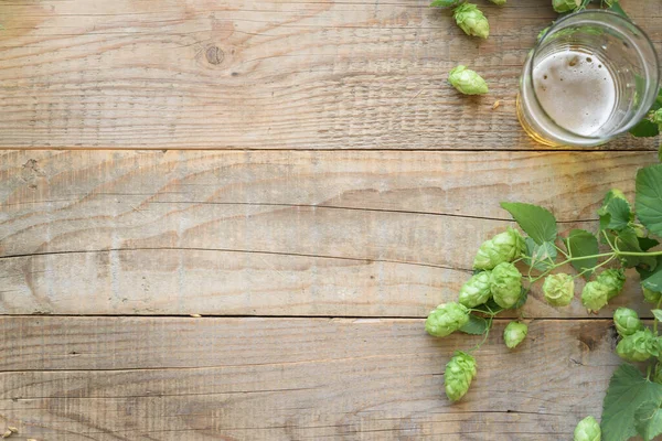 Yeşil Zıplama Konileri Tahta Arka Planda Bir Bardak Bira — Stok fotoğraf