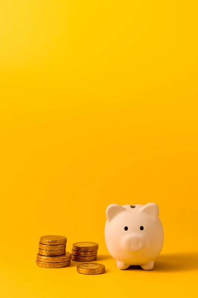 White piggy bank and coins on yellow color background. Saving, money accumulation, investment, banking or business services, wealth concept. Copy space advertising mock up