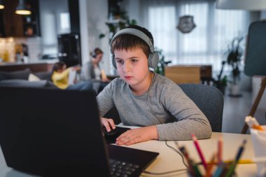 Evde masa başında otururken dizüstü bilgisayar kullanan ciddi bir çocuk. Teknoloji, eğitim, uzaklık öğrenme kavramı