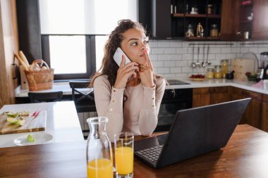 Mutfakta masada otururken cep telefonu kullanan genç bir kadın. 