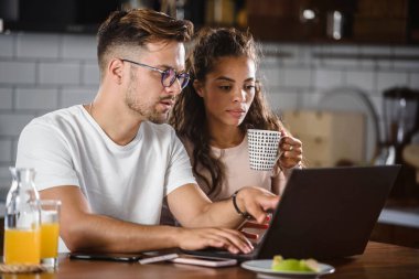 Kadın ve erkek kahvaltı yaparken dizüstü bilgisayardan bir şey izliyorlar.