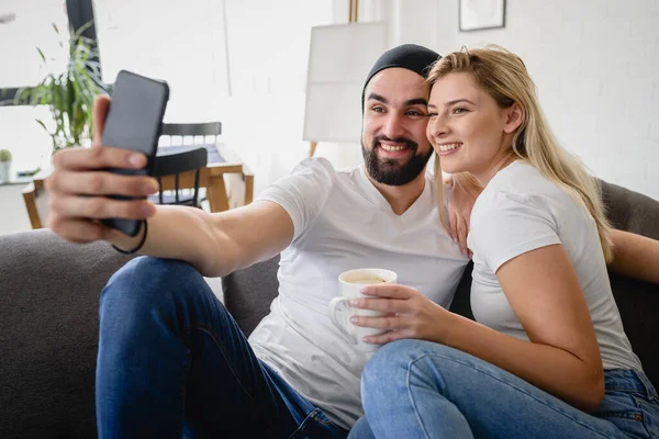 一对年轻的嬉皮士夫妇坐在家里的沙发上 用智能手机拍照 — 图库照片