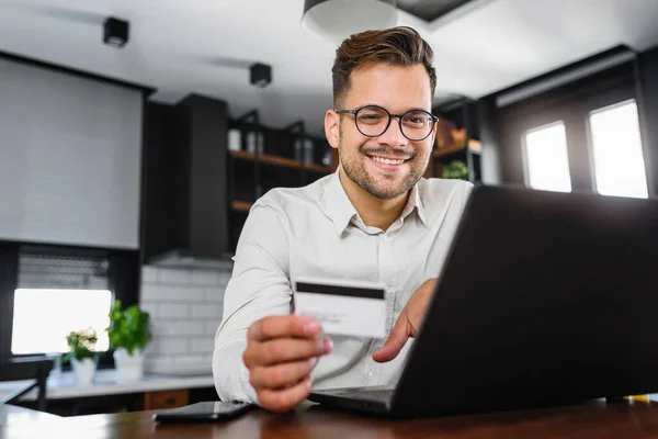 stock image Young man holding credit card sitting in front of laptop computer at home, paying for online order. People, lifestyle, modern technologies and e-commerce concept. Online banking