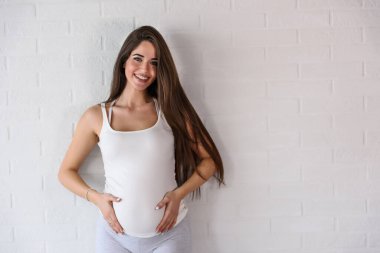 Genç ve güzel hamile bir kadın tuğla duvarın üzerinde duruyor.