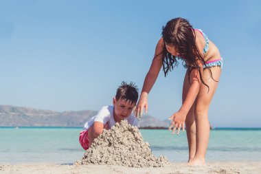 Abi ve kız kardeş sahilde kumdan kale yapıyorlar.