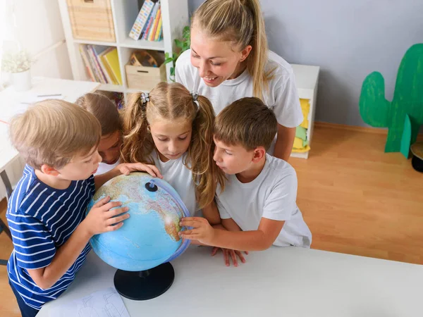 stock image group of cute children sitting aroung the globe with teacher